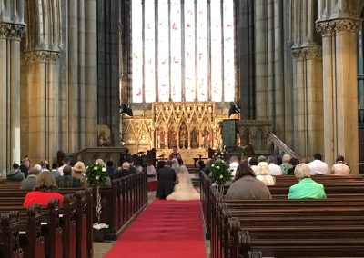 The Vicar blesses a newly married couple during their wedding ceremony. The couple kneel at the front of the Minster aisle surrounded by friends and family.
